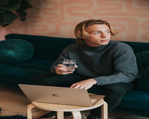 Person drinking a glass of water while looking away from laptop screen